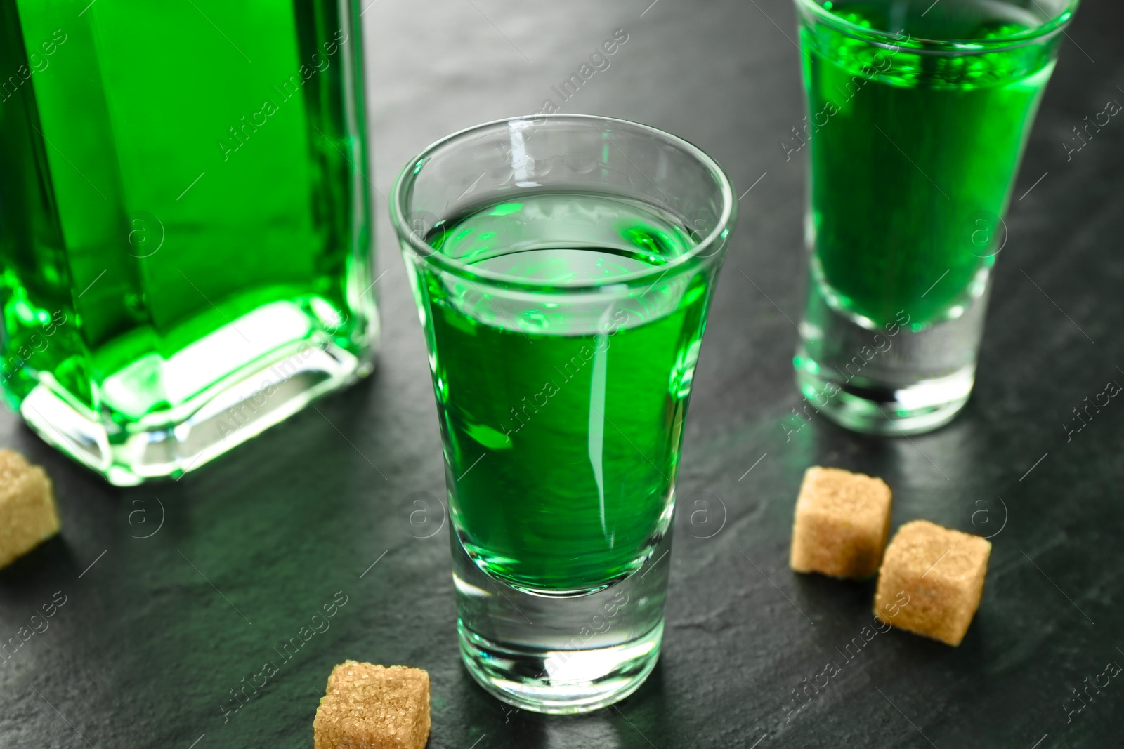 Photo of Delicious absinthe and brown sugar cubes on grey textured table, closeup