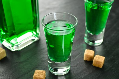 Photo of Delicious absinthe and brown sugar cubes on grey textured table, closeup