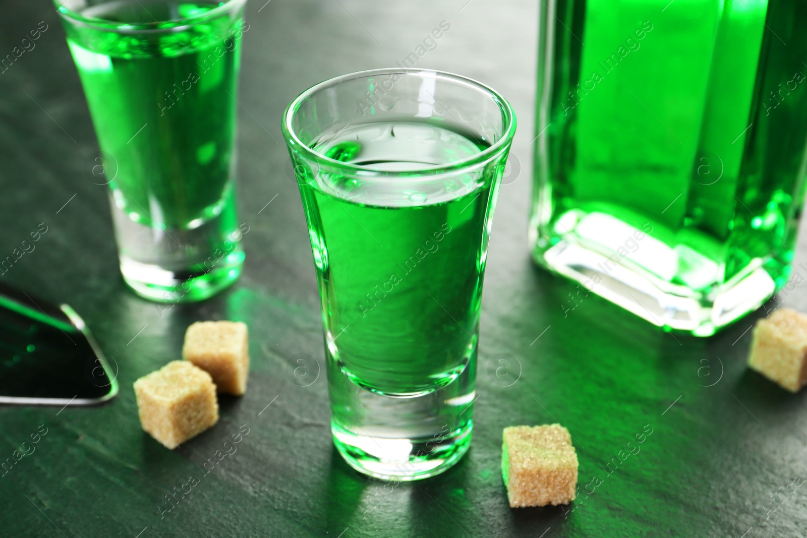 Photo of Delicious absinthe and brown sugar cubes on grey textured table, closeup