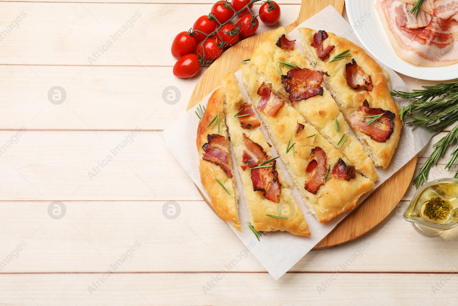 Photo of Slices of delicious focaccia bread with bacon, rosemary, oil and tomatoes on wooden table, flat lay. Space for text