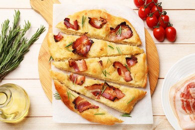 Photo of Slices of delicious focaccia bread with bacon, rosemary, oil and tomatoes on wooden table, flat lay