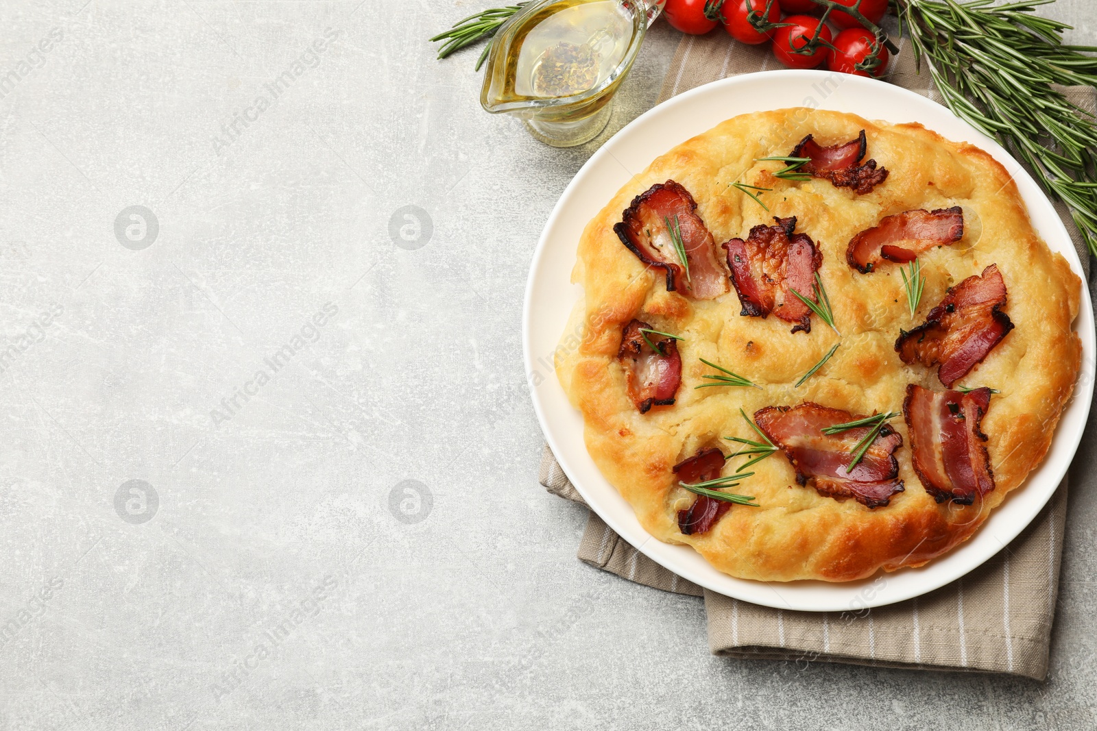 Photo of Delicious focaccia bread with bacon, rosemary, tomatoes and oil on light grey table, flat lay. Space for text