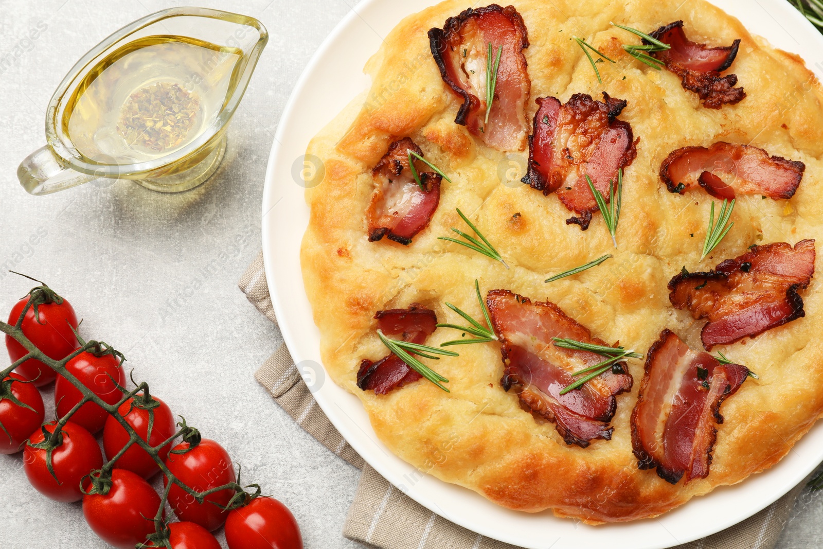 Photo of Delicious focaccia bread with bacon, rosemary, tomatoes and oil on light grey table, flat lay