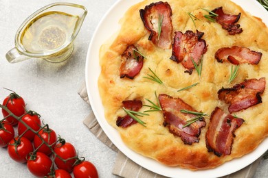 Photo of Delicious focaccia bread with bacon, rosemary, tomatoes and oil on light grey table, flat lay