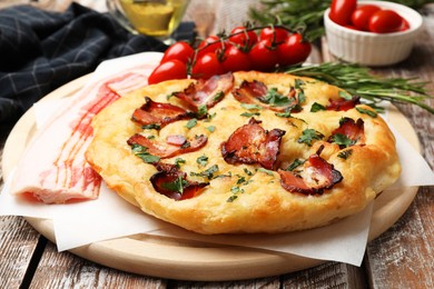 Photo of Delicious focaccia bread with bacon, parsley, tomatoes and rosemary on wooden table, closeup