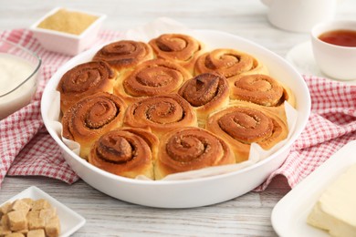 Photo of Freshly baked cinnamon rolls and ingredients on light wooden table, closeup