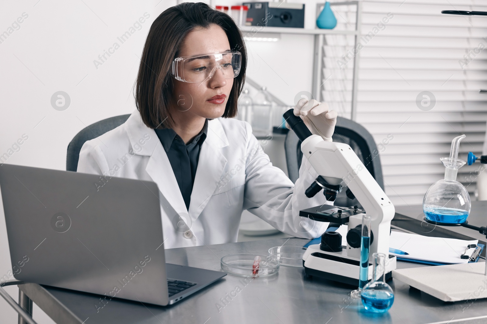 Photo of Scientist with microscope and laptop working at table in laboratory