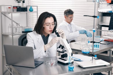 Photo of Scientist with microscope and laptop working at table in laboratory