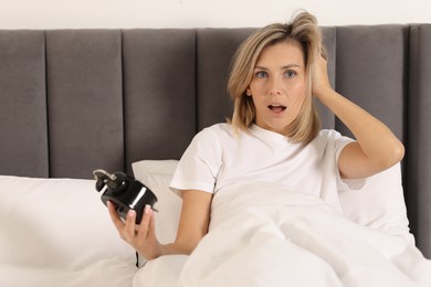 Overslept woman with alarm clock in bed at home