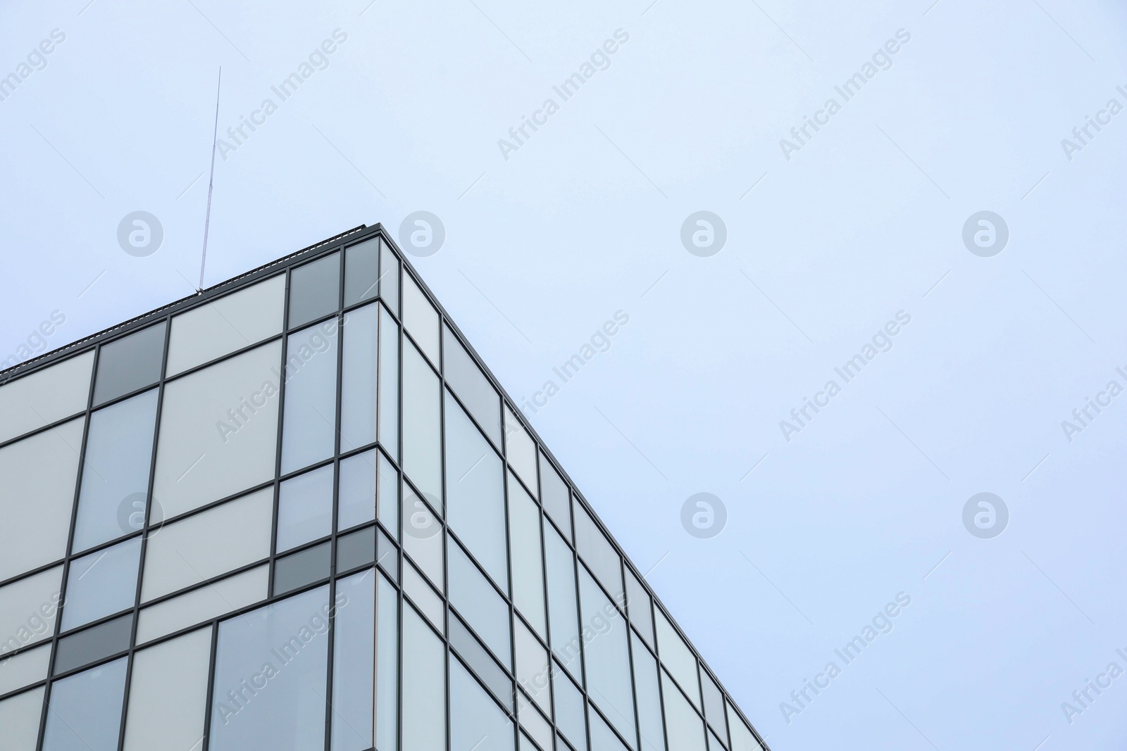 Photo of Modern building with many windows against blue sky, low angle view. Space for text