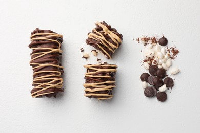 Delicious chocolate puffed rice bars and cacao chips on white table, flat lay