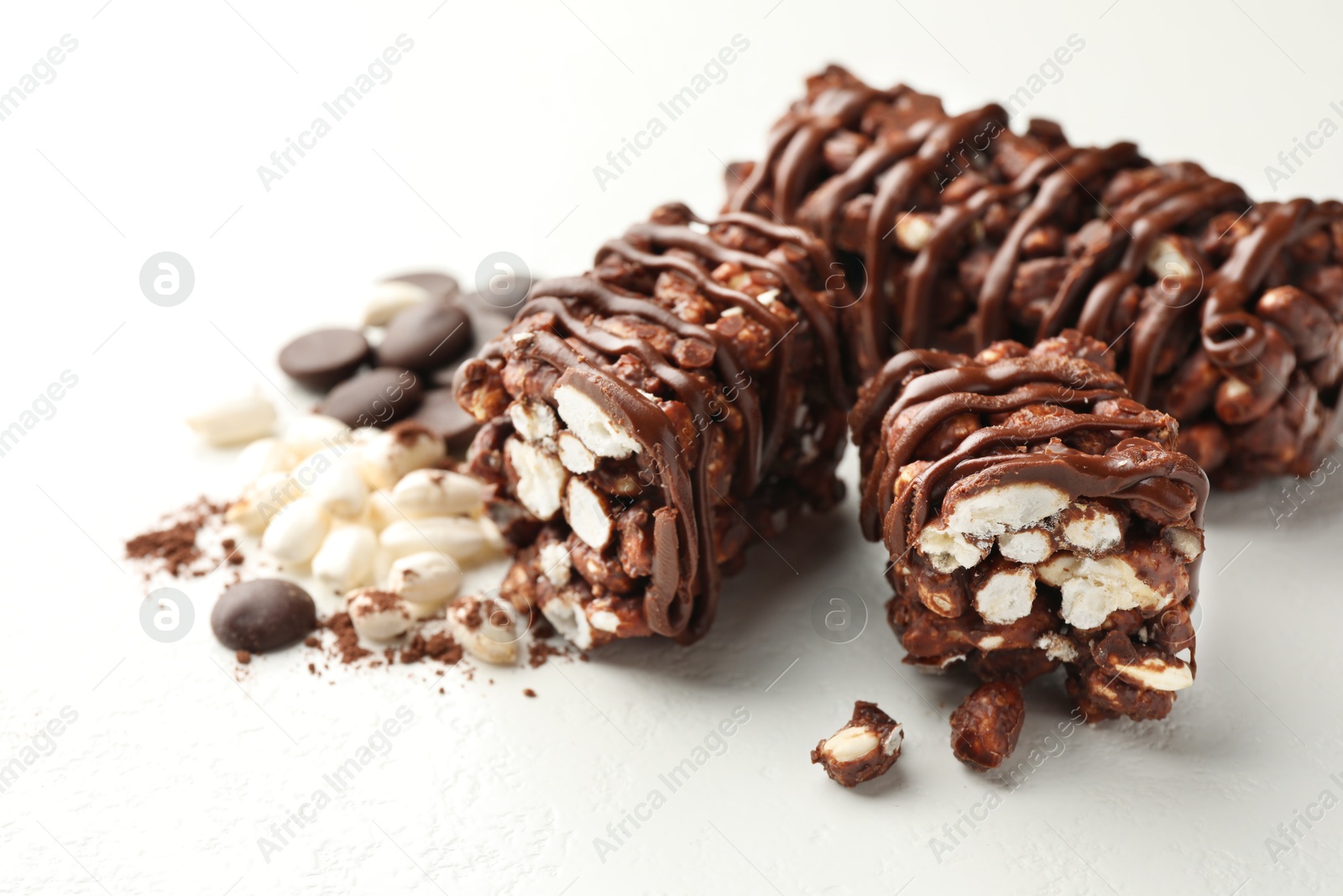 Photo of Delicious chocolate puffed rice bars and cacao chips on white table, closeup