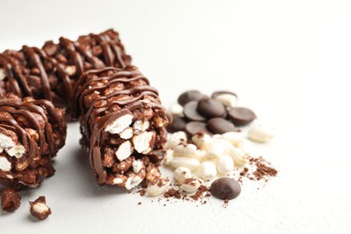 Photo of Delicious chocolate puffed rice bars and cacao chips on white table, closeup