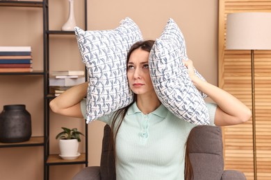 Photo of Annoyed woman covering her ears with pillows due to loud sound at home