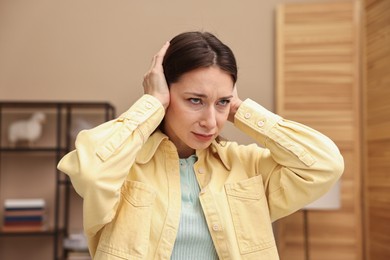 Photo of Annoyed woman covering her ears due to loud sound at home