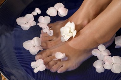 Photo of Woman soaking her feet in bowl with water and flowers, closeup. Spa treatment