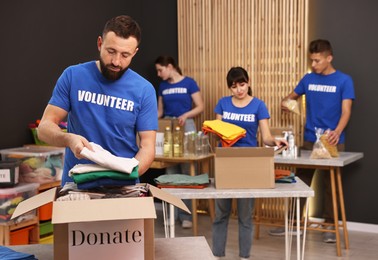 Photo of Group of volunteers packing donation goods at tables indoors, selective focus