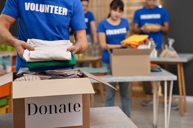 Volunteer putting clothes into donation box indoors, closeup