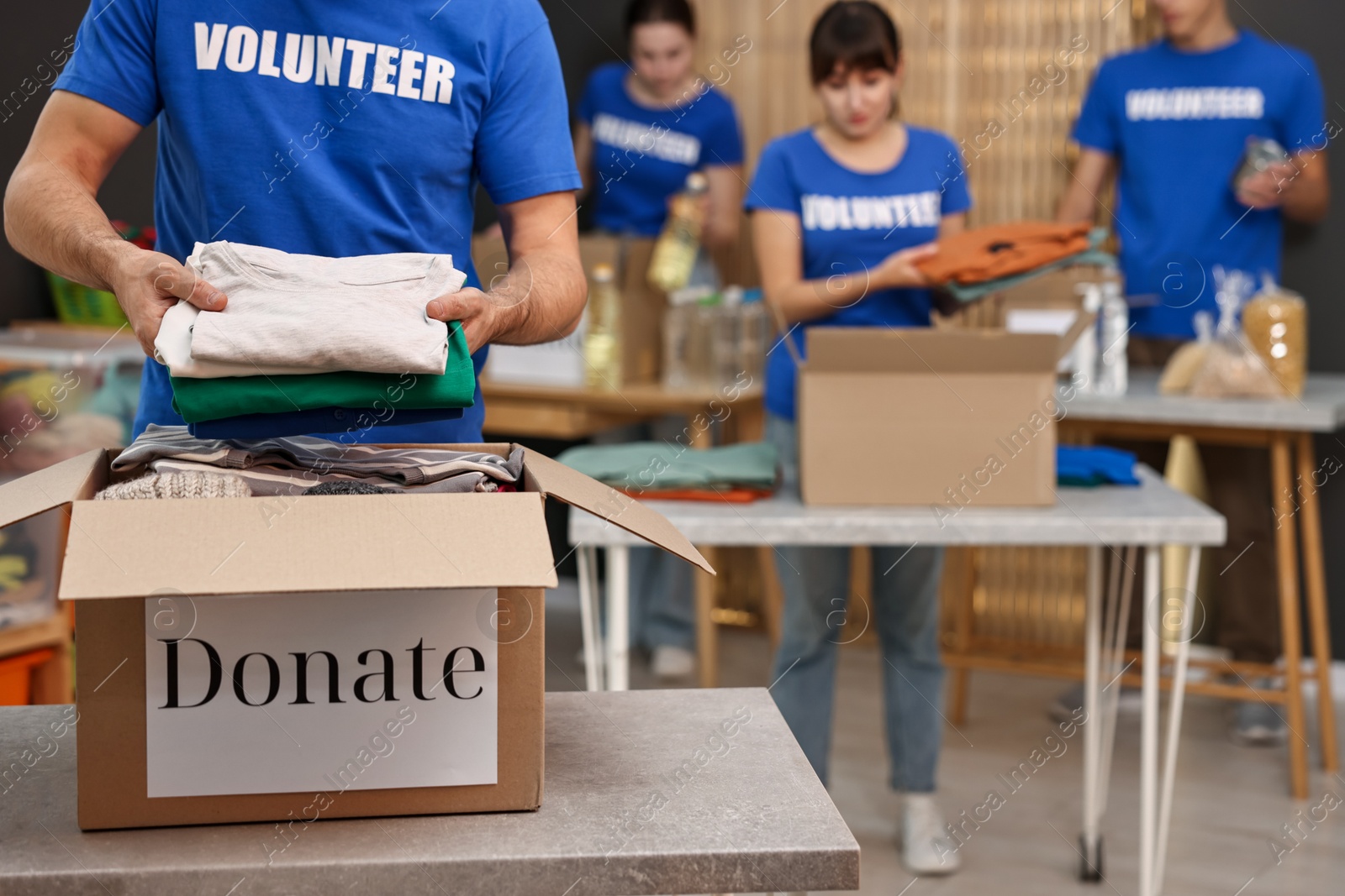 Photo of Group of volunteers packing donation goods at tables indoors, selective focus