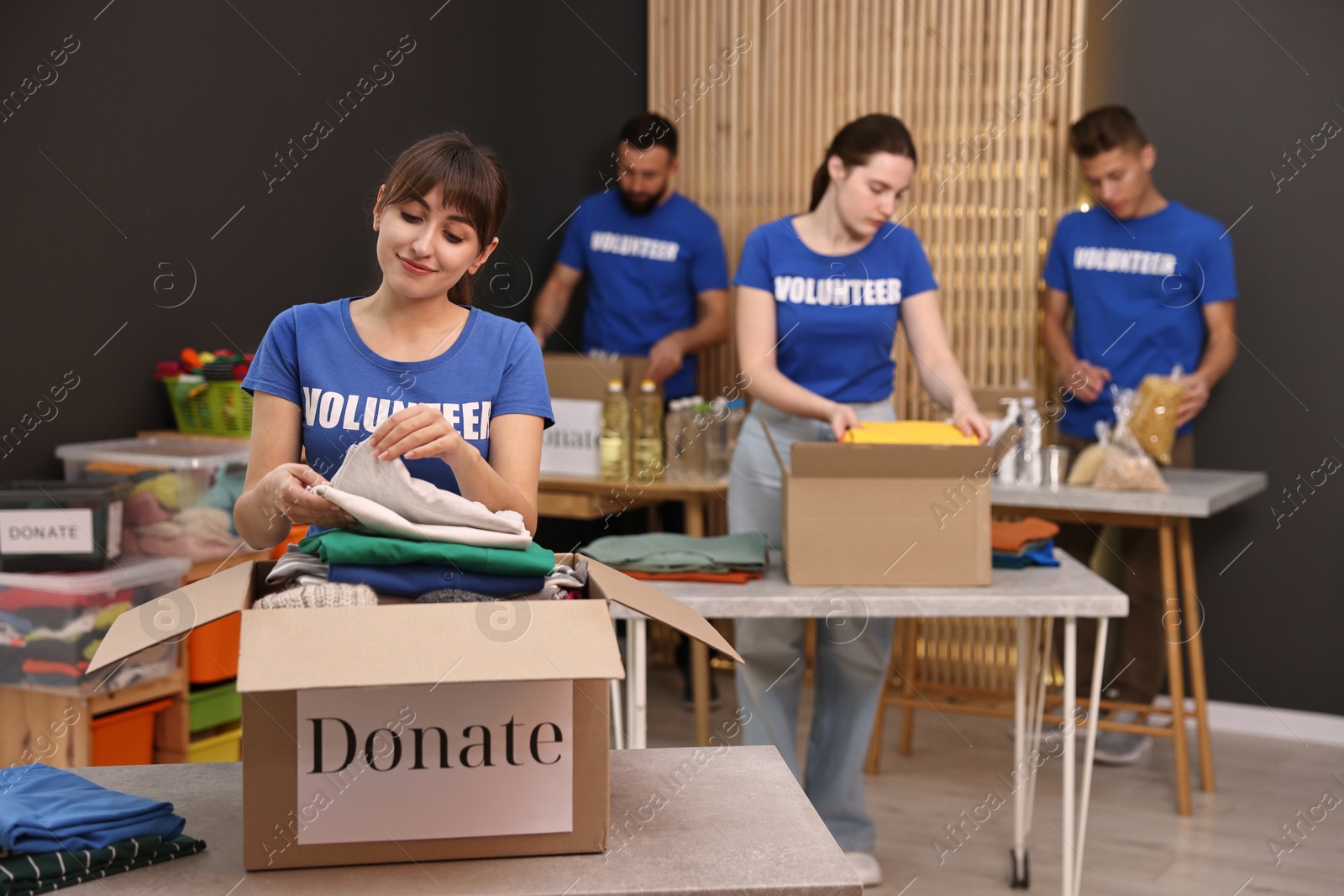 Photo of Group of volunteers packing donation goods at tables indoors, selective focus