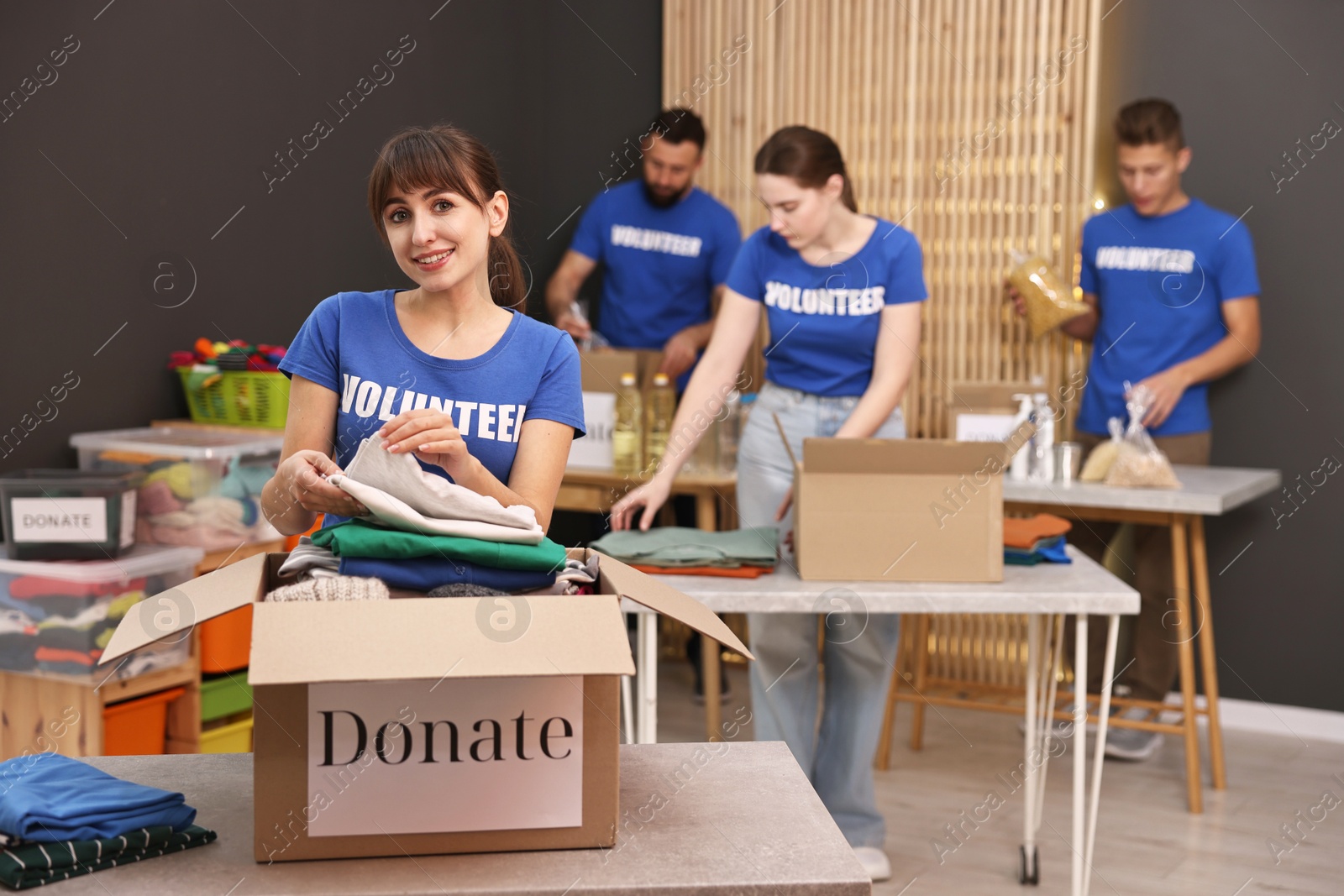 Photo of Group of volunteers packing donation goods at tables indoors, selective focus