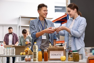 Photo of Volunteers packing food donations at tables indoors, selective focus