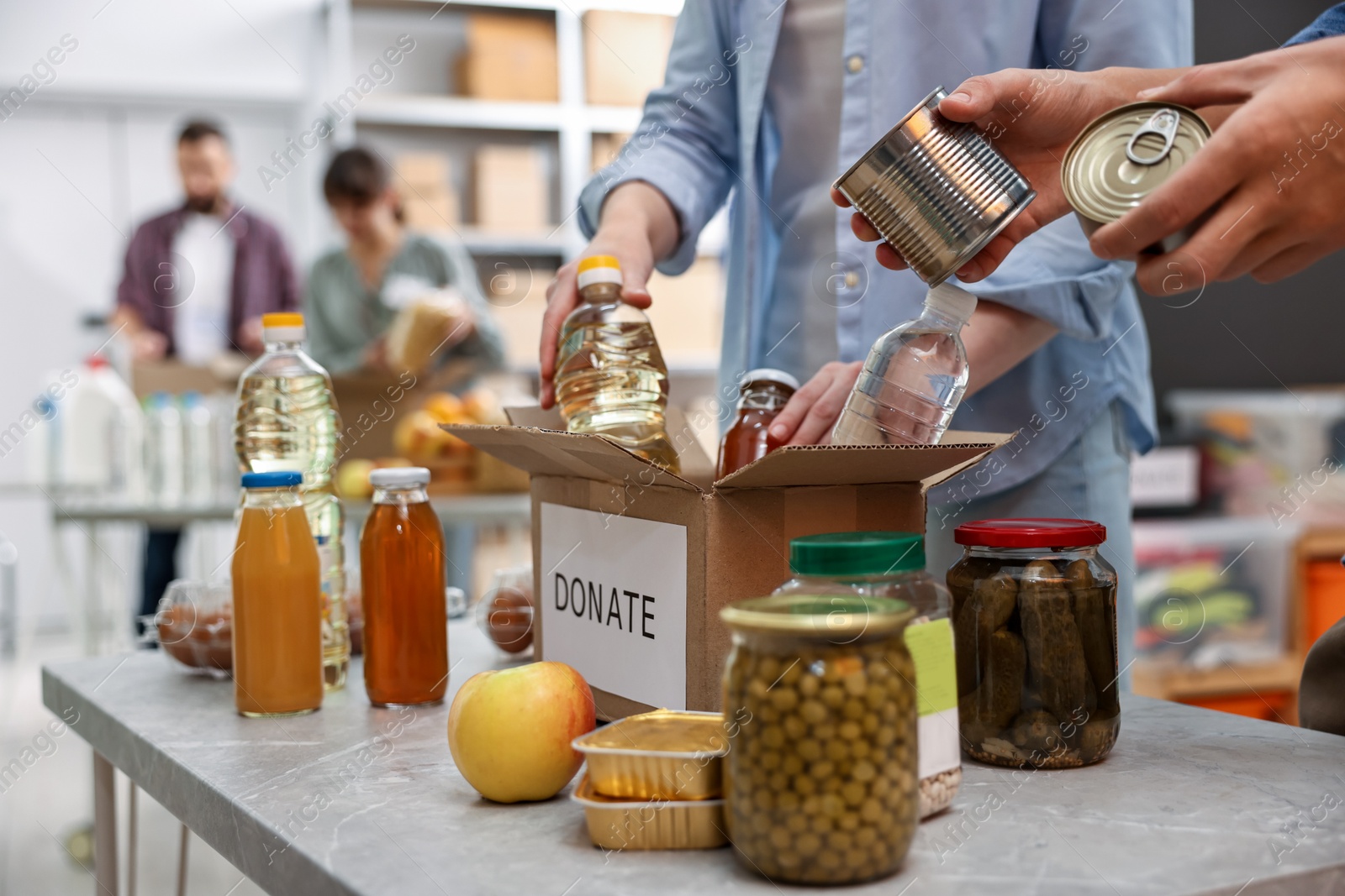 Photo of Volunteers packing food donations at table indoors, closeup