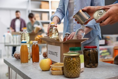 Photo of Volunteers packing food donations at table indoors, closeup