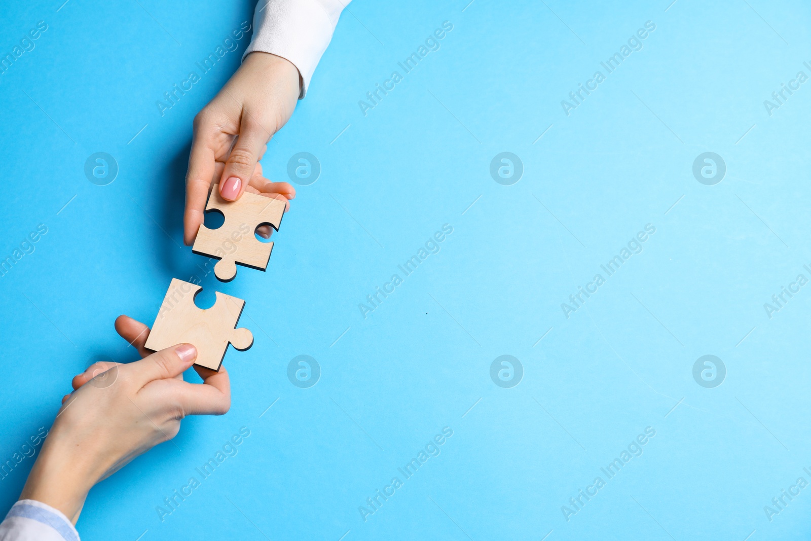 Photo of Business strategy and teamwork concept. Partners putting puzzle pieces together on light blue background, top view. Space for text