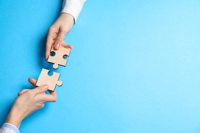 Photo of Business strategy and teamwork concept. Partners putting puzzle pieces together on light blue background, top view. Space for text