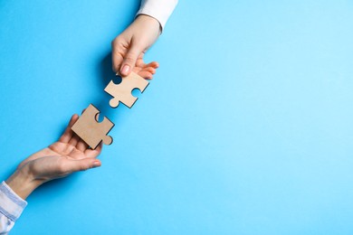 Photo of Business strategy and teamwork concept. Partners putting puzzle pieces together on light blue background, top view. Space for text