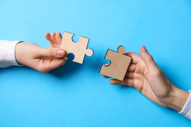 Photo of Business strategy and teamwork concept. Partners putting puzzle pieces together on light blue background, closeup