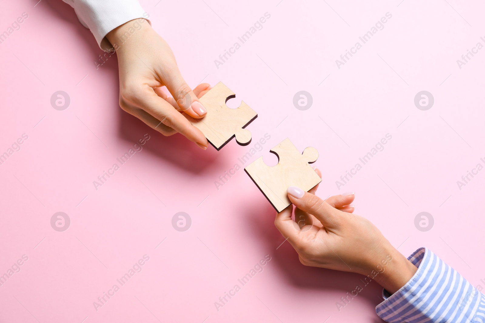 Photo of Business strategy and teamwork concept. Partners putting puzzle pieces together on pink background, top view