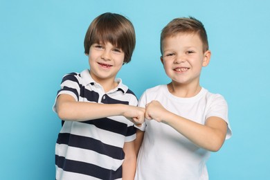 Photo of Cute brothers making fist bump on light blue background