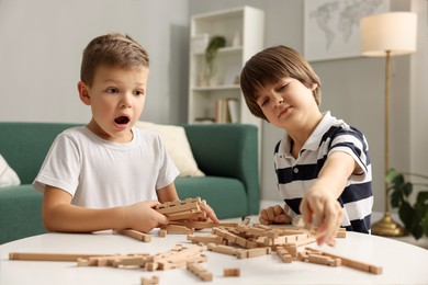 Photo of Cute brothers playing with wooden construction set at table indoors