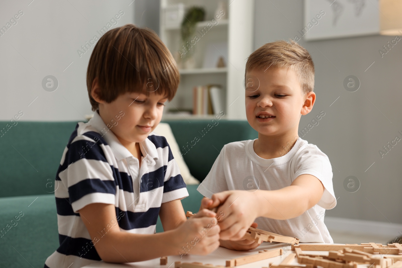 Photo of Cute brothers playing with wooden construction set at table indoors