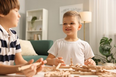 Photo of Cute brothers playing with wooden construction set at table indoors