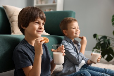 Photo of Cute brothers with glasses of milk and cookies at home, selective focus