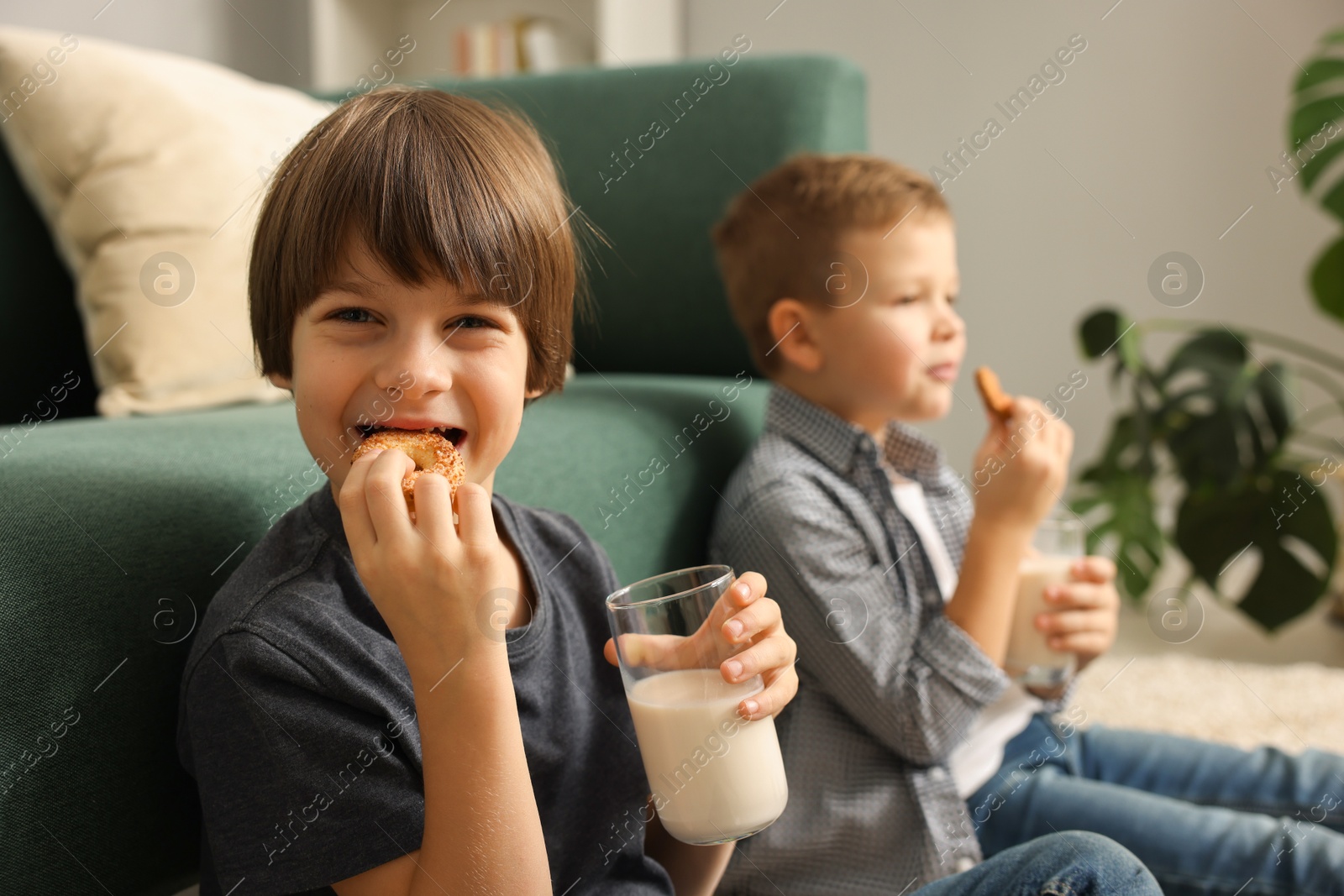 Photo of Cute brothers with glasses of milk and cookies at home, selective focus