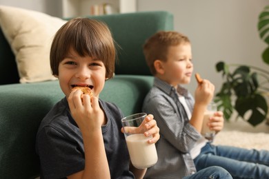 Cute brothers with glasses of milk and cookies at home, selective focus