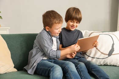 Photo of Cute brothers using tablet on sofa at home