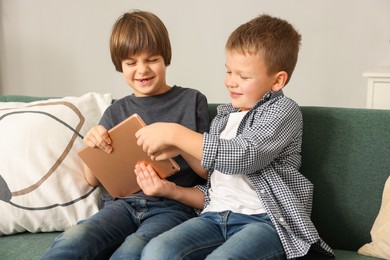 Photo of Cute brothers taking away tablet from each other on sofa at home