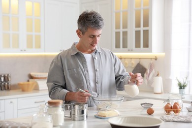 Making dough. Man pouring milk into bowl at white marble table in kitchen