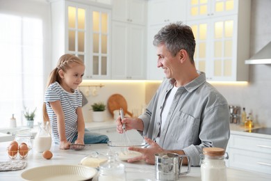 Photo of Father and his daughter making dough at white marble table in kitchen