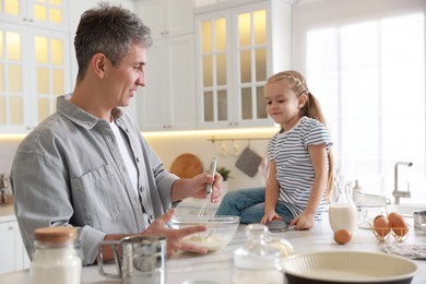 Photo of Father and his daughter making dough at white marble table in kitchen