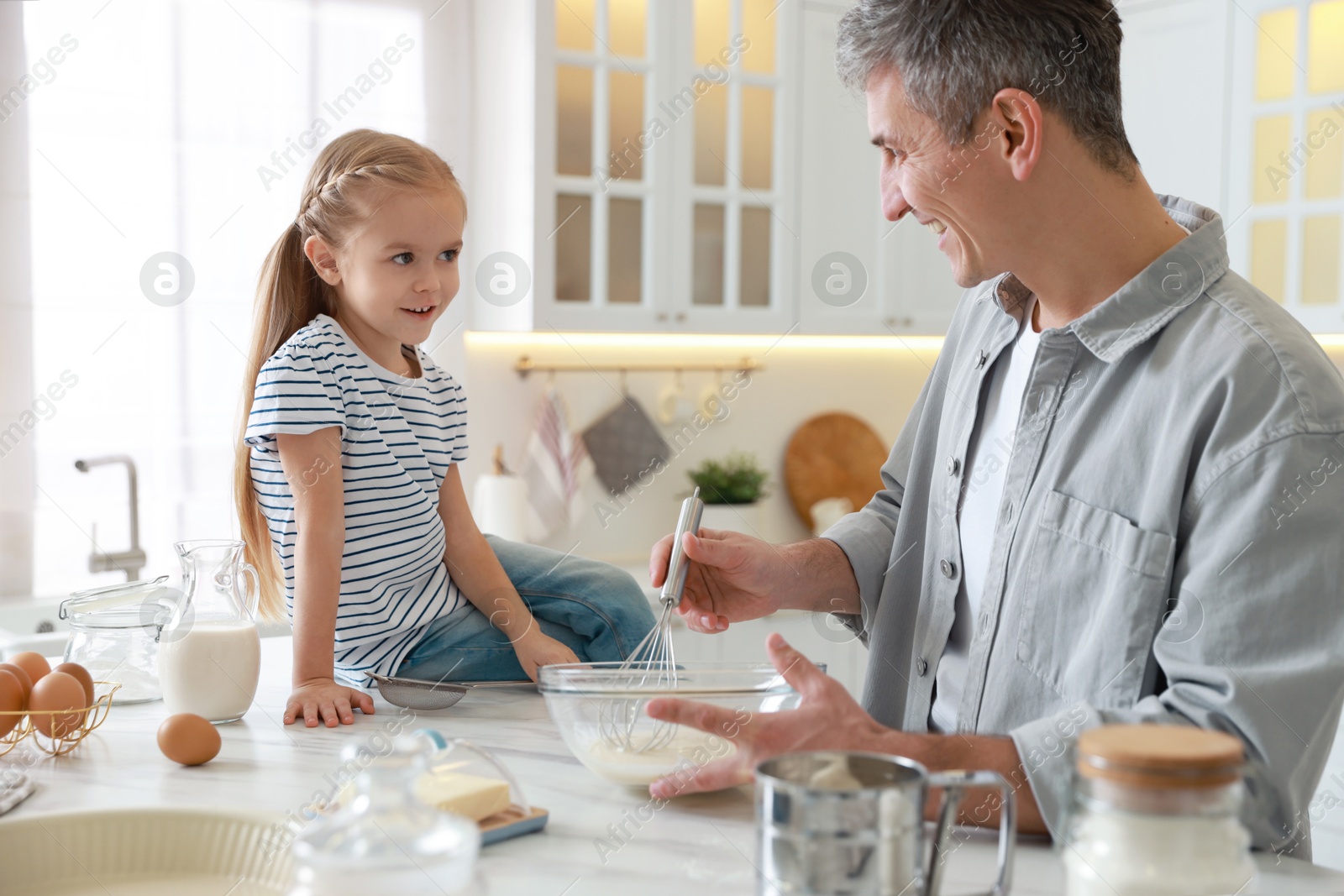 Photo of Father and his daughter making dough at white marble table in kitchen