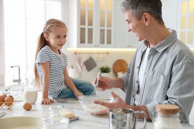 Photo of Father and his daughter making dough at white marble table in kitchen