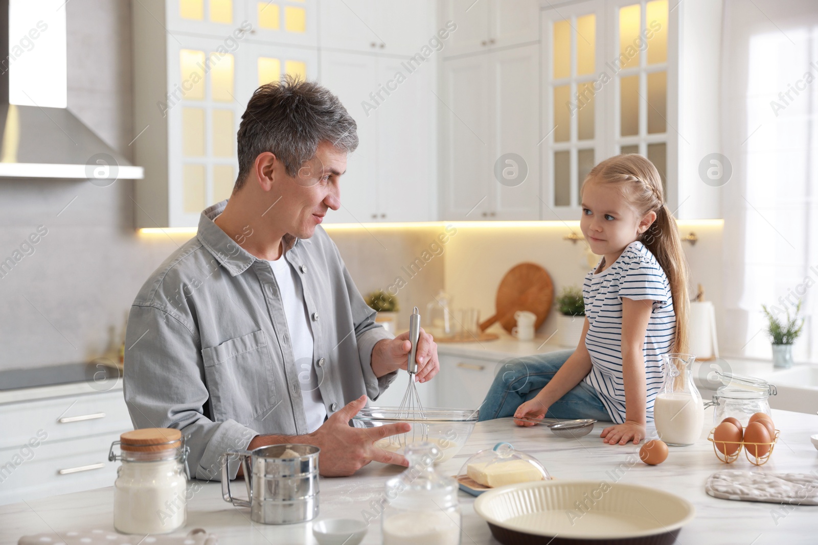 Photo of Father and his daughter making dough at white marble table in kitchen