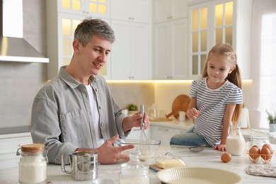 Photo of Father and his daughter making dough at white marble table in kitchen