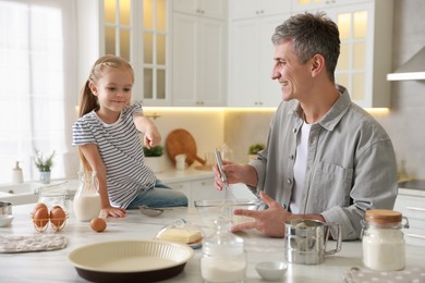 Photo of Father and his daughter making dough at white marble table in kitchen